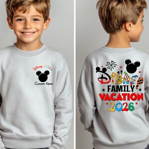 May include: A light gray sweatshirt featuring a black Mickey Mouse silhouette and the text "Disney 2026" in red, green, and black. The back of the sweatshirt displays "Disney Family Vacation 2026" with Mickey Mouse and friends.