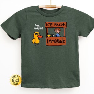 May include: Dark green t-shirt featuring a cartoon duck asking "Got any Grapes?" next to a lemonade stand with the text "ICE FRESH Lemonade." The shirt is made of a soft material and is suitable for children.