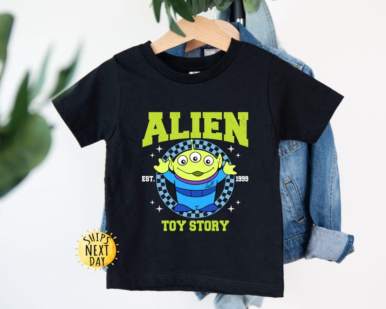 Puede incluir: Camiseta negra con un personaje extraterrestre verde de Toy Story. La camiseta tiene el texto "Alien" en un arco amarillo sobre el personaje y "Toy Story" debajo del personaje. El texto "Est. 1999" est&aacute; en blanco debajo del arco.