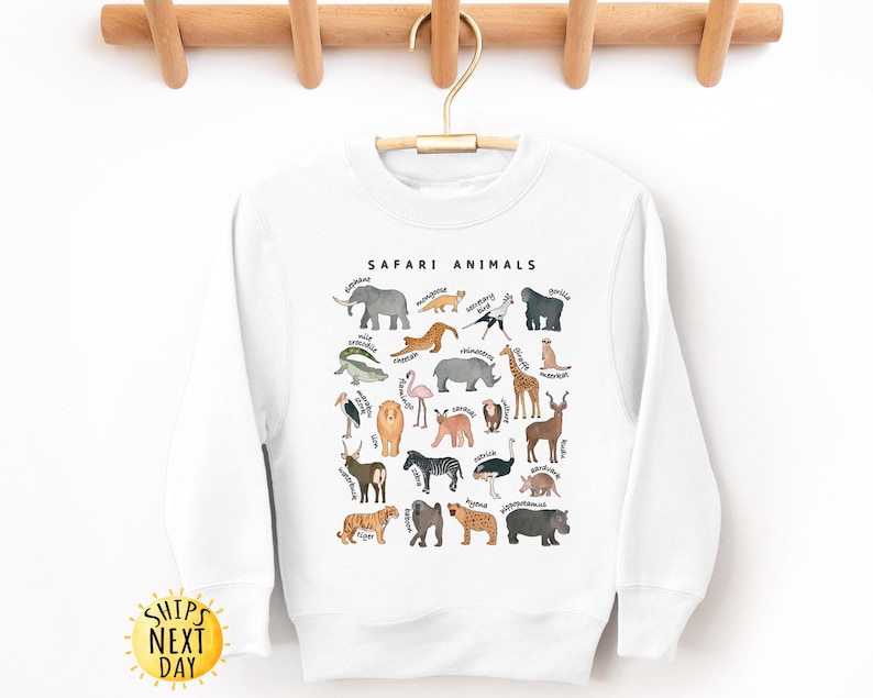 May include: White sweatshirt with a graphic of safari animals, including a giraffe, elephant, lion, zebra, and more. The text "SAFARI ANIMALS" is printed above the graphic.