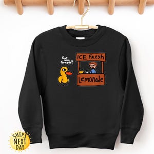 May include: Black sweatshirt with a cartoon duck asking "Got any Grapes?" and a lemonade stand graphic that says "ICE FRESH Lemonade." The sweatshirt has a crew neck and long sleeves. The design is in yellow, orange, brown, and blue.