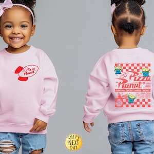 Puede incluir: Sudadera rosa claro con el logo de Pizza Planet en rojo en la parte delantera. La parte trasera de la sudadera tiene un dise&ntilde;o m&aacute;s grande con el logo de Pizza Planet, personajes alien&iacute;genas y texto sobre un fondo a cuadros rojos y blancos.