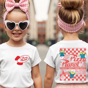Puede incluir: Camiseta blanca con el logo rojo de Pizza Planet en la parte delantera y un gr&aacute;fico en la parte trasera. El gr&aacute;fico trasero incluye el texto "Pizza Planet" y extraterrestres de dibujos animados. La camiseta la lleva un ni&ntilde;o.