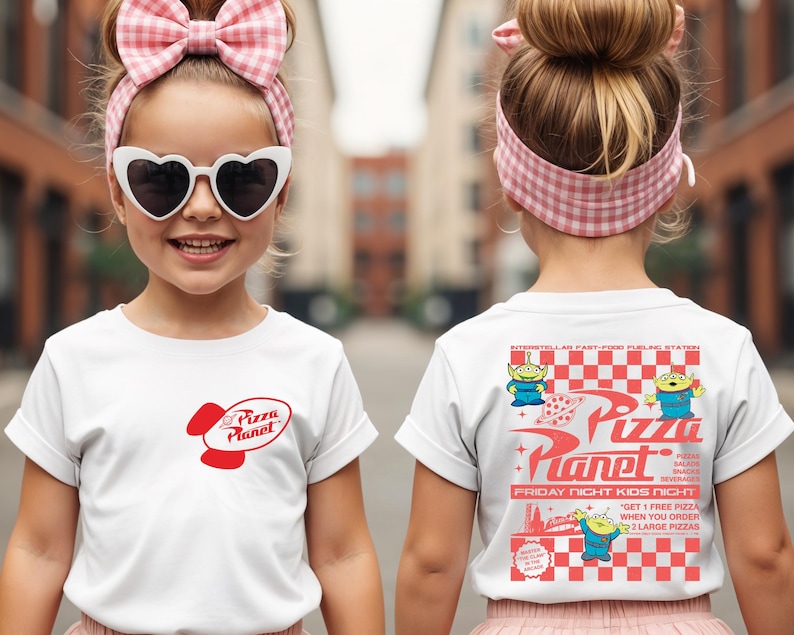 Puede incluir: Camiseta blanca con el logo rojo de Pizza Planet en la parte delantera y un gr&aacute;fico en la parte trasera. El gr&aacute;fico trasero incluye el texto "Pizza Planet" y extraterrestres de dibujos animados. La camiseta la lleva un ni&ntilde;o.