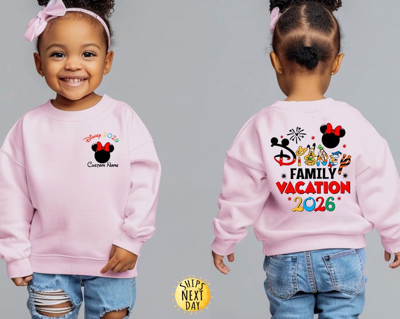 May include: A light pink sweatshirt with a Minnie Mouse graphic and the text "Disney 2026" on the front. The back of the sweatshirt features the text "Disney Family Vacation 2026" with various Disney character illustrations.