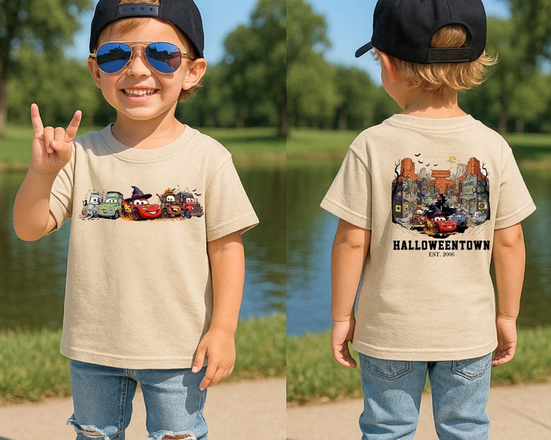 K&ouml;nnte beinhalten: Beiges kurz&auml;rmeliges T-Shirt mit einem Halloween-Motiv auf Vorder- und R&uuml;ckseite. Die Vorderseite zeigt Cartoon-Autos in Halloween-Kost&uuml;men. Die R&uuml;ckseite zeigt eine Stadtlandschaft mit dem Text "Halloweentown Est. 2006".