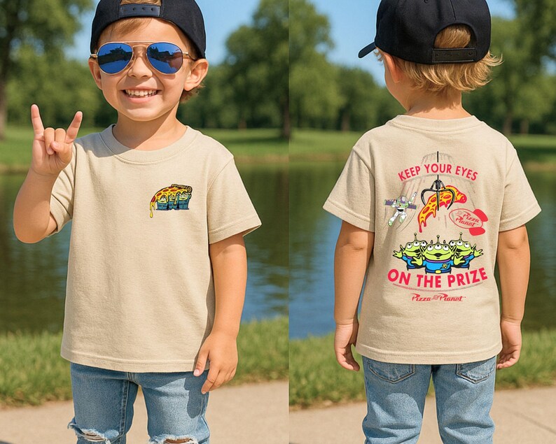 May include: Tan t-shirt featuring a pizza slice graphic on the front and the text "Keep Your Eyes on the Prize" with alien characters on the back. The shirt is worn by a child wearing a black cap and blue jeans.