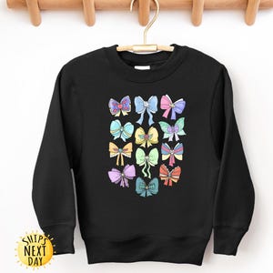 May include: Black sweatshirt with a colorful graphic of bows. The bows are in various colors and designs, including pink, blue, yellow, and green.