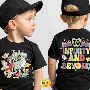 May include: Black t-shirt featuring a colourful graphic of Toy Story characters, including Woody, Buzz Lightyear, Rex, and a unicorn. The back of the shirt has the text "To Infinity and Beyond" in a rainbow font.