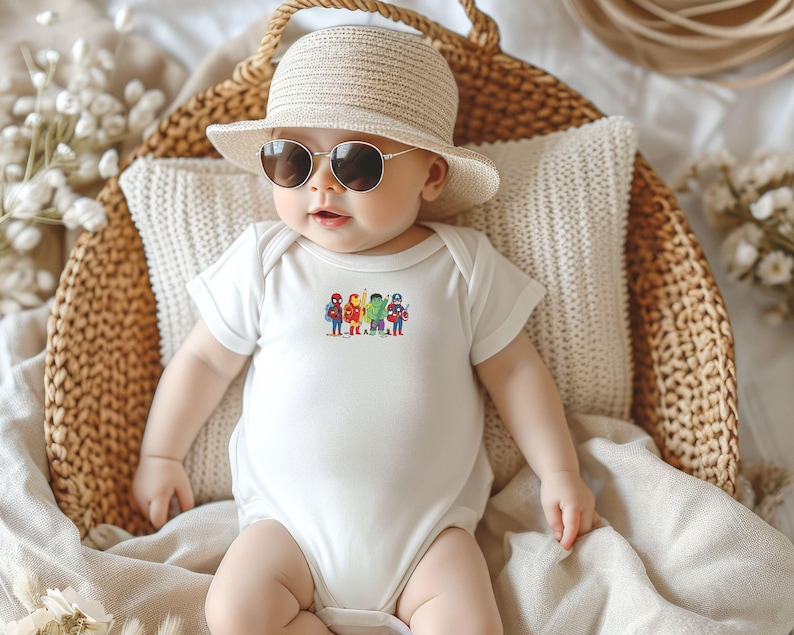 May include: A baby wearing a white bodysuit with a colorful graphic of superheroes. The baby is also wearing a straw hat and sunglasses, and is sitting in a woven basket.