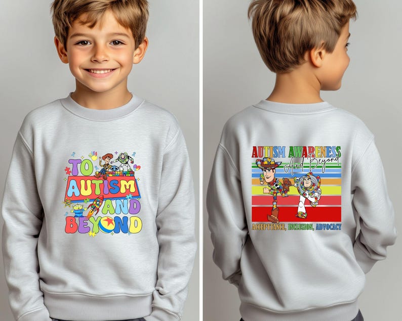 K&ouml;nnte beinhalten: Ein hellgraues Sweatshirt mit dem Schriftzug "TO AUTISM AND BEYOND" und bunten Zeichentrickfiguren. Auf der R&uuml;ckseite des Sweatshirts steht "AUTISM AWARENESS And Beyond" mit Zeichentrickfiguren und einem Regenbogenstreifen-Design.