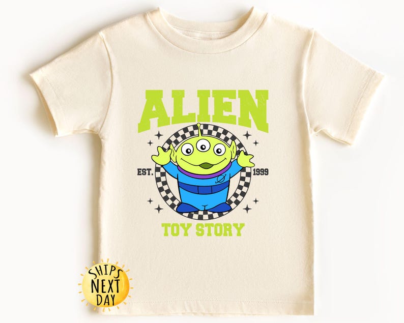 Puede incluir: Una camiseta verde claro con un personaje extraterrestre verde de Toy Story. La camiseta tiene el texto "ALIEN" en letras verdes sobre el extraterrestre y "EST. 1999" y "TOY STORY" debajo del extraterrestre.