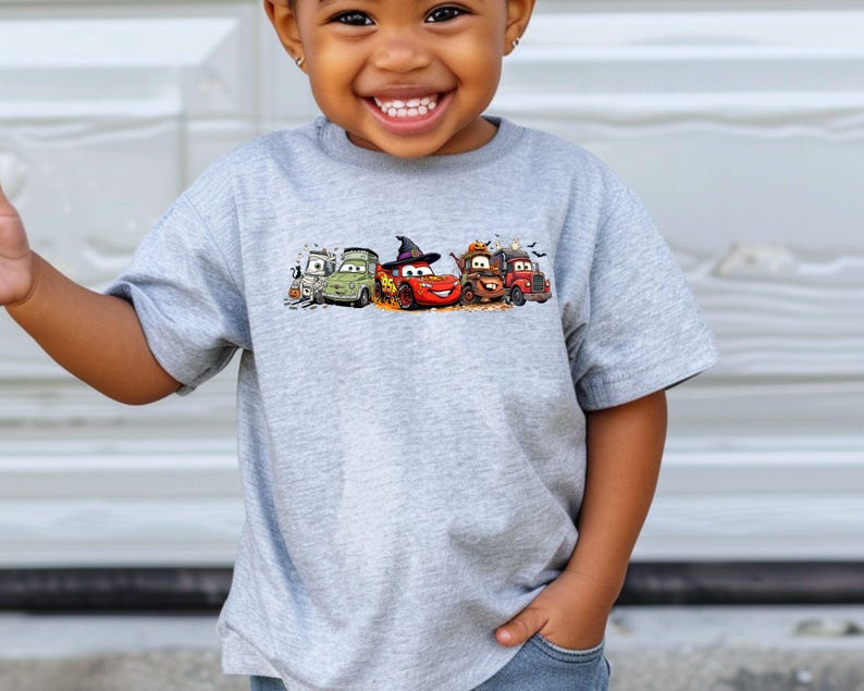 K&ouml;nnte beinhalten: Hellgraues T-Shirt mit einem Cartoon-Motiv von Autos zum Thema Halloween. Die Autos sind rot, gr&uuml;n und braun. Das T-Shirt wird von einem kleinen Kind getragen.