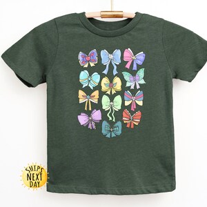 May include: A dark green t-shirt with a colorful bow pattern. The bows are in various colors, including pink, blue, yellow, and green.
