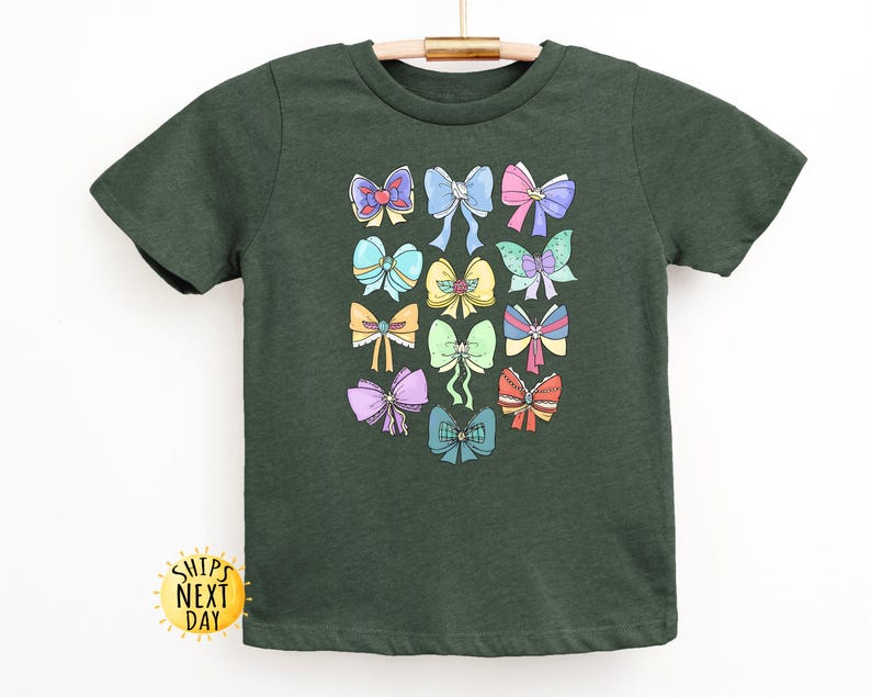 May include: A dark green t-shirt with a colorful bow pattern. The bows are in various colors, including pink, blue, yellow, and green.