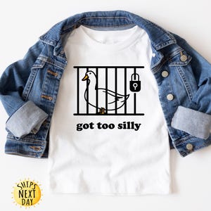 May include: White t-shirt with a black and white illustration of a duck in a cage with a padlock. The text "got too silly" is printed below the image.
