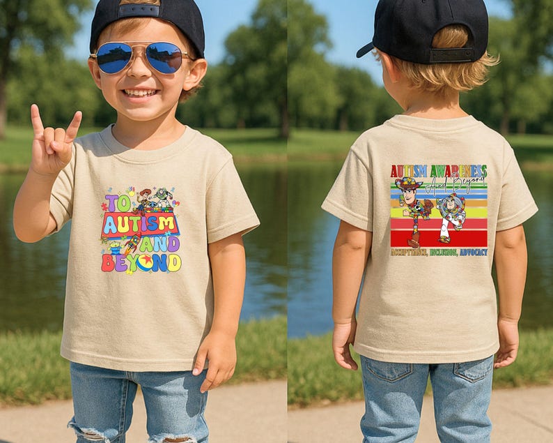K&ouml;nnte beinhalten: Beiges kurz&auml;rmeliges T-Shirt mit einem farbenfrohen Aufdruck auf der Vorderseite mit dem Text "To Autism and Beyond" und Zeichentrickfiguren. Auf der R&uuml;ckseite des Shirts befindet sich ein Aufdruck mit der Aufschrift "Autism Awareness and Beyond".