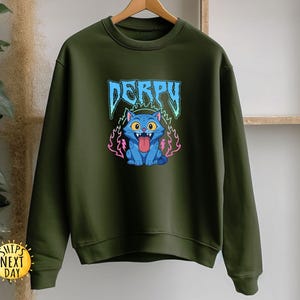 May include: An olive green sweatshirt with a cartoon cat design. The cat is blue with yellow eyes and a pink tongue. The word "DERPY" is above the cat in blue and white lettering. The cat is surrounded by pink and purple flames.