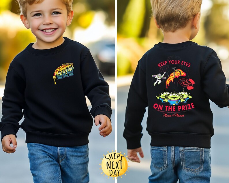 May include: Black sweatshirt featuring a colorful graphic of the Pizza Planet aliens and pizza slice. The back of the sweatshirt has the text "KEEP YOUR EYES ON THE PRIZE" and more graphics. The sweatshirt is worn by a child.
