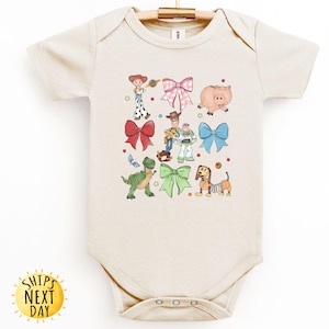 May include: A beige baby onesie with a print of Toy Story characters, including Woody, Buzz Lightyear, Rex, and Slinky Dog. The characters are surrounded by colorful bows.