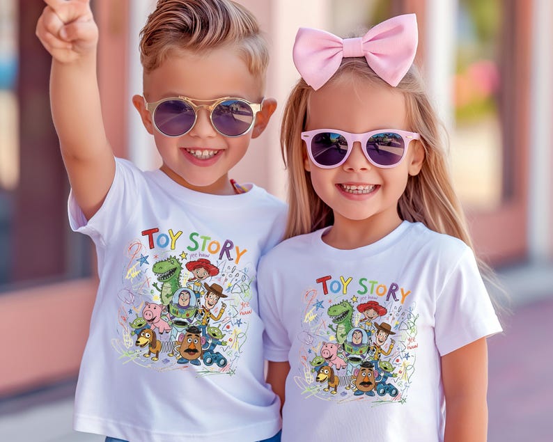 May include: Two white short-sleeved t-shirts featuring a colorful graphic print of Toy Story characters including Woody, Buzz Lightyear, Rex, and Mr. Potato Head, with the text Toy Story printed in a multi-colored font above the character illustration.