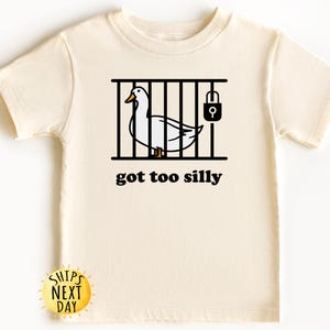May include: A white t-shirt with a black illustration of a duck in a cage with a padlock. The text "got too silly" is printed below the illustration.