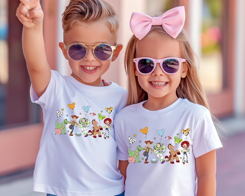 May include: Two children wearing white t-shirts with a colorful Toy Story graphic. The graphic features cartoon characters like Woody, Buzz Lightyear, and others. Both children are wearing sunglasses and smiling.