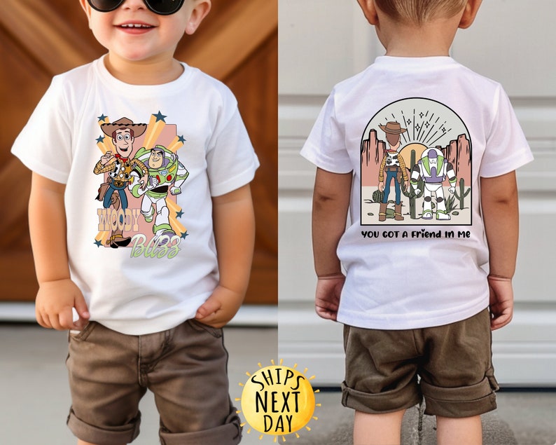 K&ouml;nnte beinhalten: Wei&szlig;es T-Shirt mit einem Cartoon-Bild von Woody und Buzz Lightyear aus Toy Story. Die Vorderseite des Shirts tr&auml;gt den Schriftzug "Woody Buzz". Die R&uuml;ckseite des Shirts zeigt ein Cartoon-Bild von Woody und Buzz Lightyear in einer W&uuml;stenlandschaft mit dem Text "You got a friend in me".