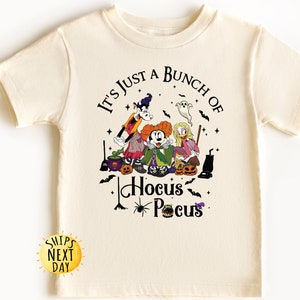 May include: A cream colored t-shirt with a black graphic of Mickey Mouse, Donald Duck, and Goofy dressed as witches. The graphic includes the text "It's just a bunch of Hocus Pocus".