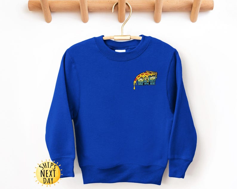May include: Royal blue sweatshirt with a crew neck. The sweatshirt features a small, colorful graphic of a pizza slice with a cartoon face. The sweatshirt is hanging on a wooden hanger.
