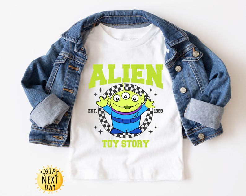 Puede incluir: Camiseta blanca con un personaje extraterrestre verde de Toy Story. La camiseta tiene el texto "Alien" en letras verdes con un patr&oacute;n a cuadros y el texto "Toy Story" debajo.