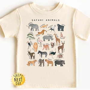 May include: A cream-colored t-shirt with a graphic of safari animals and their names. The animals are illustrated in a cartoon style with watercolor-like details. The text "SAFARI ANIMALS" is printed in black at the top of the graphic.