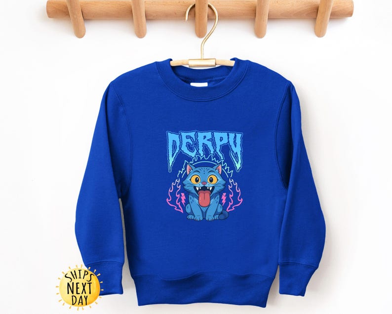 May include: Royal blue sweatshirt with a cartoon cat graphic and the word "DERPY" in blue. The cat has a pink tongue and is surrounded by pink and blue flames. The sweatshirt is displayed on a wooden hanger.