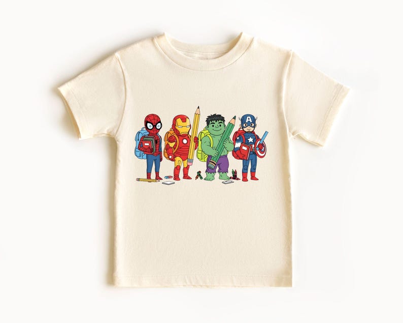 May include: Cream-colored t-shirt featuring a cartoon illustration of four superheroes: Spider-Man, Iron Man, Hulk, and Captain America, each holding a pencil and wearing a backpack. The superheroes are in their signature colors.