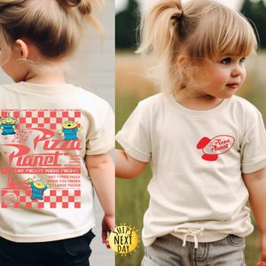 Puede incluir: Una camiseta de color crema con el logo de Pizza Planet en rojo en la parte delantera y un gr&aacute;fico m&aacute;s grande en la parte trasera. El gr&aacute;fico trasero incluye el logo de Pizza Planet, extraterrestres de dibujos animados y el texto "DAY NIGHT KIDS NIGHT".