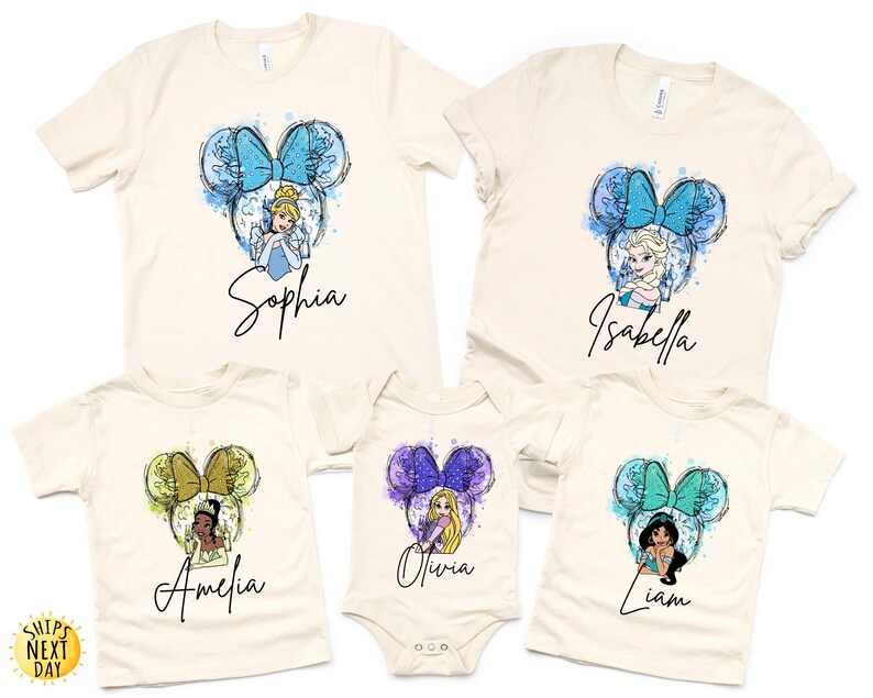 May include: A collection of five cream-colored t-shirts and one bodysuit featuring watercolor-style graphics of Disney characters inside mouse ear silhouettes. Each garment displays a unique character, a colorful bow, and a personalized name in script.