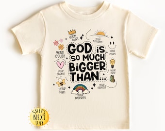 May include: A beige t-shirt with a graphic design that says "God is so much bigger than..." and includes illustrations of a crown, a heart, a bee, a sun, a lightbulb, a butterfly, a rainbow, and a smiley face. The text "Your hurt", "Your doubt", "Your shame", "Your mistakes", "Your fears", "Your past", "Your pain", "Your regrets", and "Your worries" are written around the graphic design.