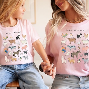 K&ouml;nnte beinhalten: Zwei Personen tragen rosa T-Shirts mit einer Grafik von Nutztieren und dem Text "Farm Animals".