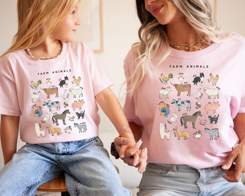 K&ouml;nnte beinhalten: Zwei Personen tragen rosa T-Shirts mit einer Grafik von Nutztieren und dem Text "Farm Animals".
