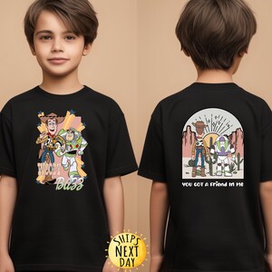 K&ouml;nnte beinhalten: Schwarzes T-Shirt mit einem Motiv von Woody und Buzz Lightyear aus Toy Story. Die Vorderseite des Shirts zeigt "Woody Buzz" und die R&uuml;ckseite "You got a friend in me".