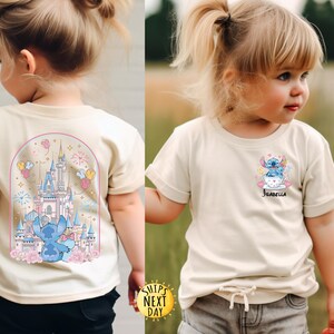 May include: Two cream-colored t-shirts featuring a cartoon character design. One shirt has a castle and character graphic on the back. The other shirt has a character graphic and the name "Isabella" on the front. Both shirts have rolled-up sleeves.