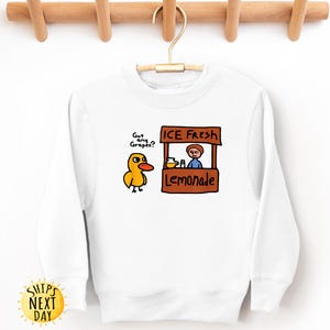 May include: White sweatshirt with a cartoon duck asking "Got any Grapes?" next to a lemonade stand that says "ICE Fresh Lemonade." The sweatshirt has long sleeves and a crew neck. A yellow sun graphic with the words "SHIPS NEXT DAY" is on the bottom left.