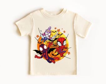 May include: Cream-coloured t-shirt with a Halloween-themed graphic. The design features three cartoon Spider-Man characters in Halloween costumes, set against a yellow moon and spiderwebs. Bats and autumn leaves complete the festive scene.