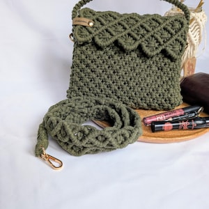 Może przedstawiać: Zielona torba z makramy w kolorze oliwkowym z pasującym paskiem na ramię. Torba ma teksturowany, geometryczny wzór i górny uchwyt. Złote okucia zdobią torbę. Do torby przymocowana jest mała skórzana metka.