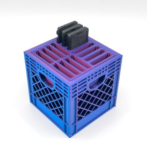 May include: A blue and purple plastic crate with a grid pattern, designed to hold and organize game cartridges. The crate has a built-in stand for the cartridges, which are visible in the image.