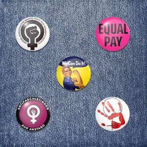 Könnte beinhalten: Fünf runde Buttons mit feministischen Slogans. Die Buttons sind pink, weiß, gelb, schwarz und weiß. Die Slogans sind "Defend Reproductive Rights! Fight for Women's Rights!", "We Can Do It!", "Equal Pay", "Antifaschistinnen Aus Anstand" und ein Handabdruck mit einem weiblichen Symbol.