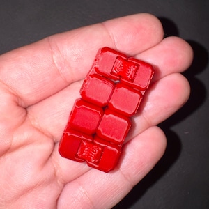 May include: A bright red fidget toy, composed of eight connected, rectangular blocks. The blocks have a textured surface and are held in a person's hand. The toy is designed to be manipulated and played with.