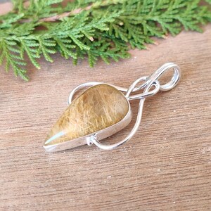 May include: A silver pendant with a teardrop-shaped golden rutilated quartz stone. The pendant has a delicate, intricate design.