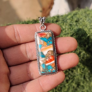 May include: A silver pendant with a rectangular turquoise, coral, and shell inlay. The pendant has a rope-like border and a silver bail.