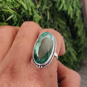 Op de afbeelding: Een zilveren ring met een grote, ovale, groene edelsteen. De ring heeft een gedetailleerde zilveren band met een parelrand.